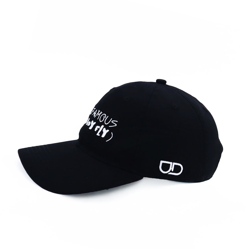 Black baseball cap with white embroidered text reading “NOT FAMOUS” on the front and a UD logo on the side.