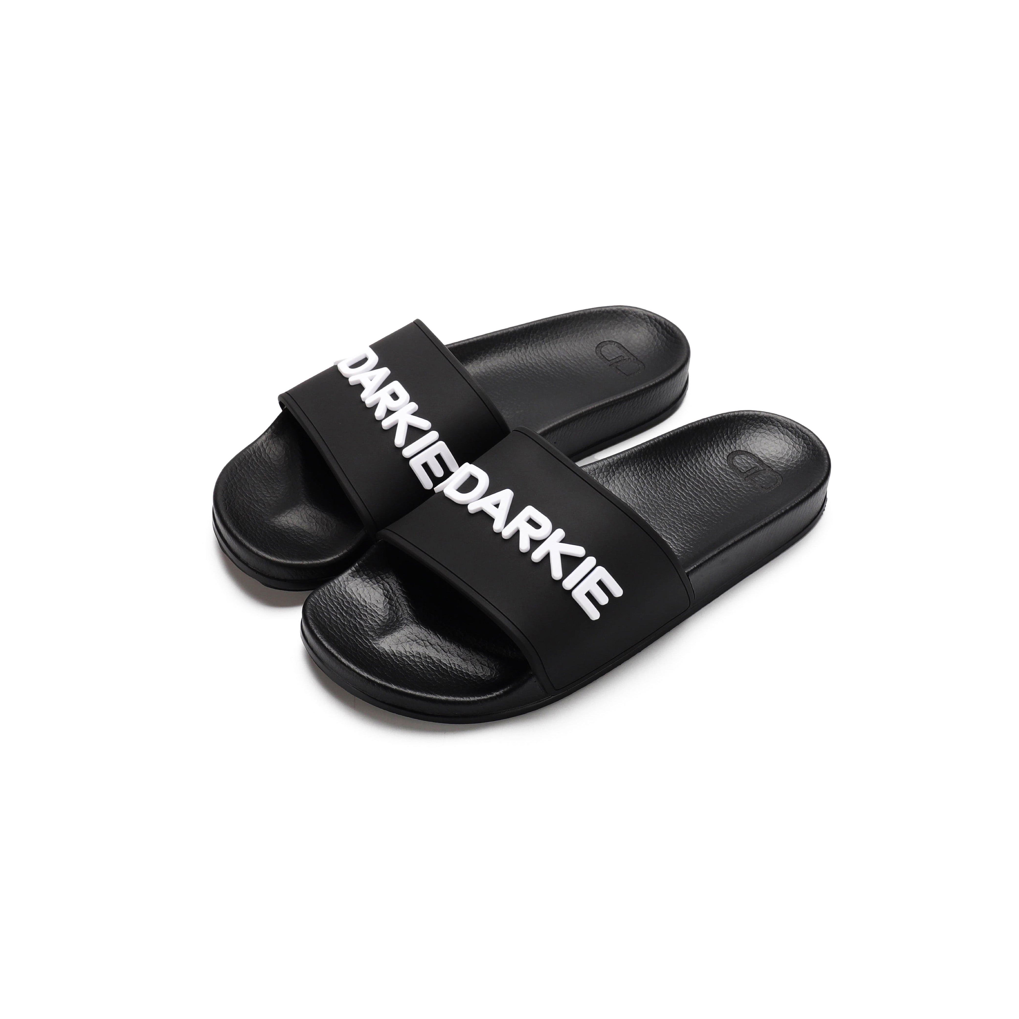Pair of black slide sandals with white silicone"UDARKIE" text across the straps. Features a simple design with textured footbed and synthetic material.