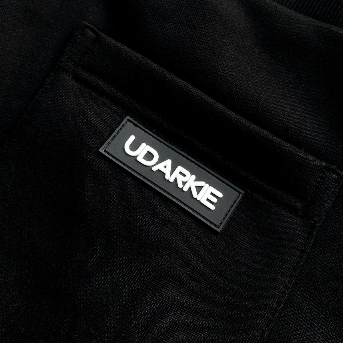 Close-up of black fabric pocket with sewn "UDARKIE" label in white text.