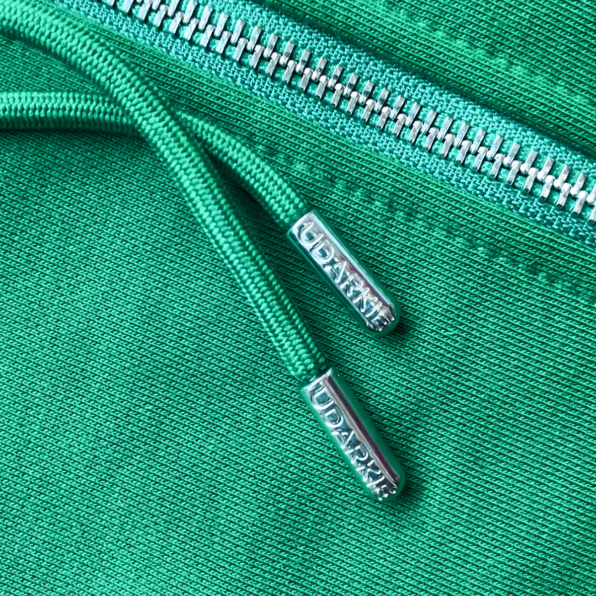 Close-up of green hoodie with silver zipper and UDARKIE branded drawcords