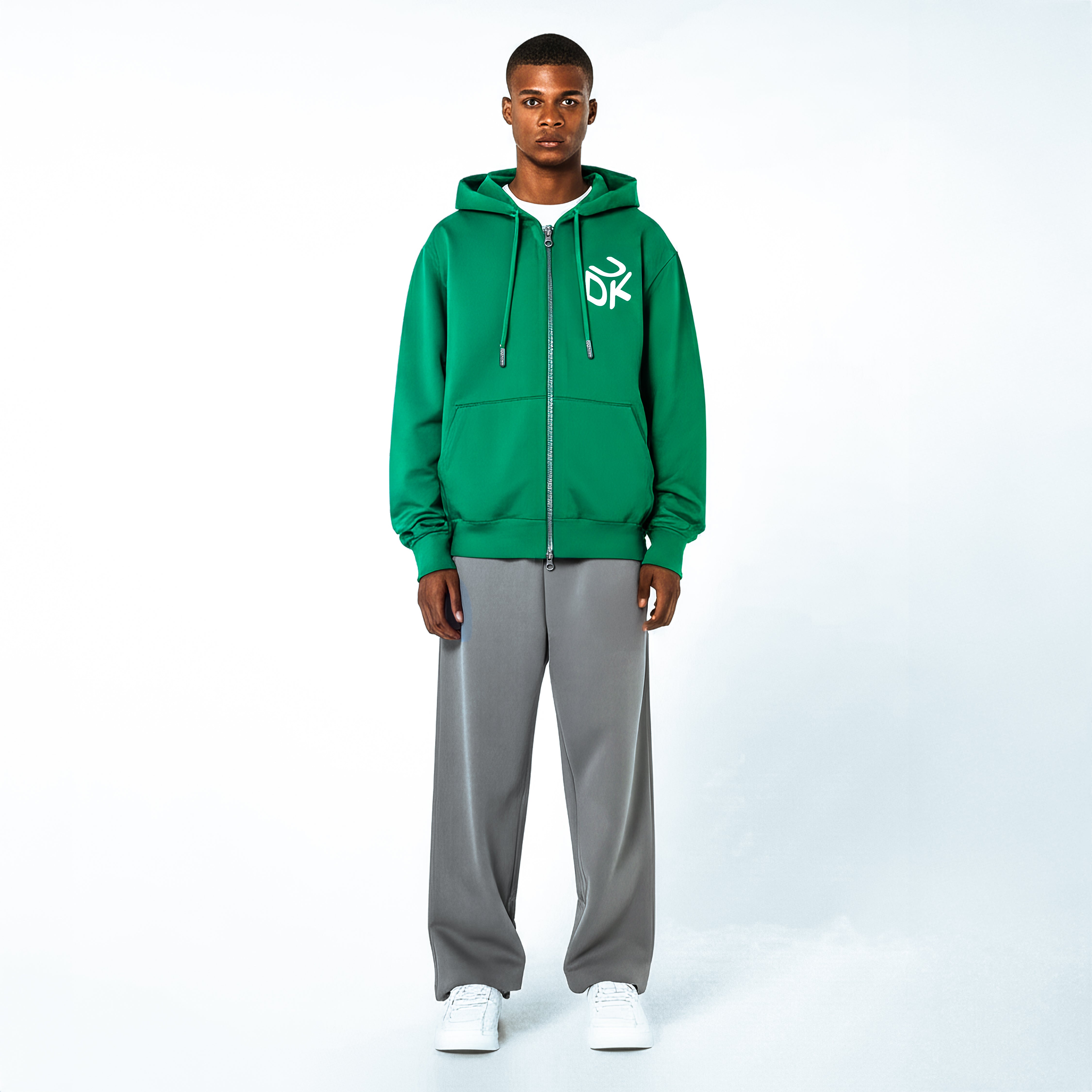 Front view of a man wearing a green zip-up hoodie with white "UDK" logo on the chest, gray pants, and white sneakers