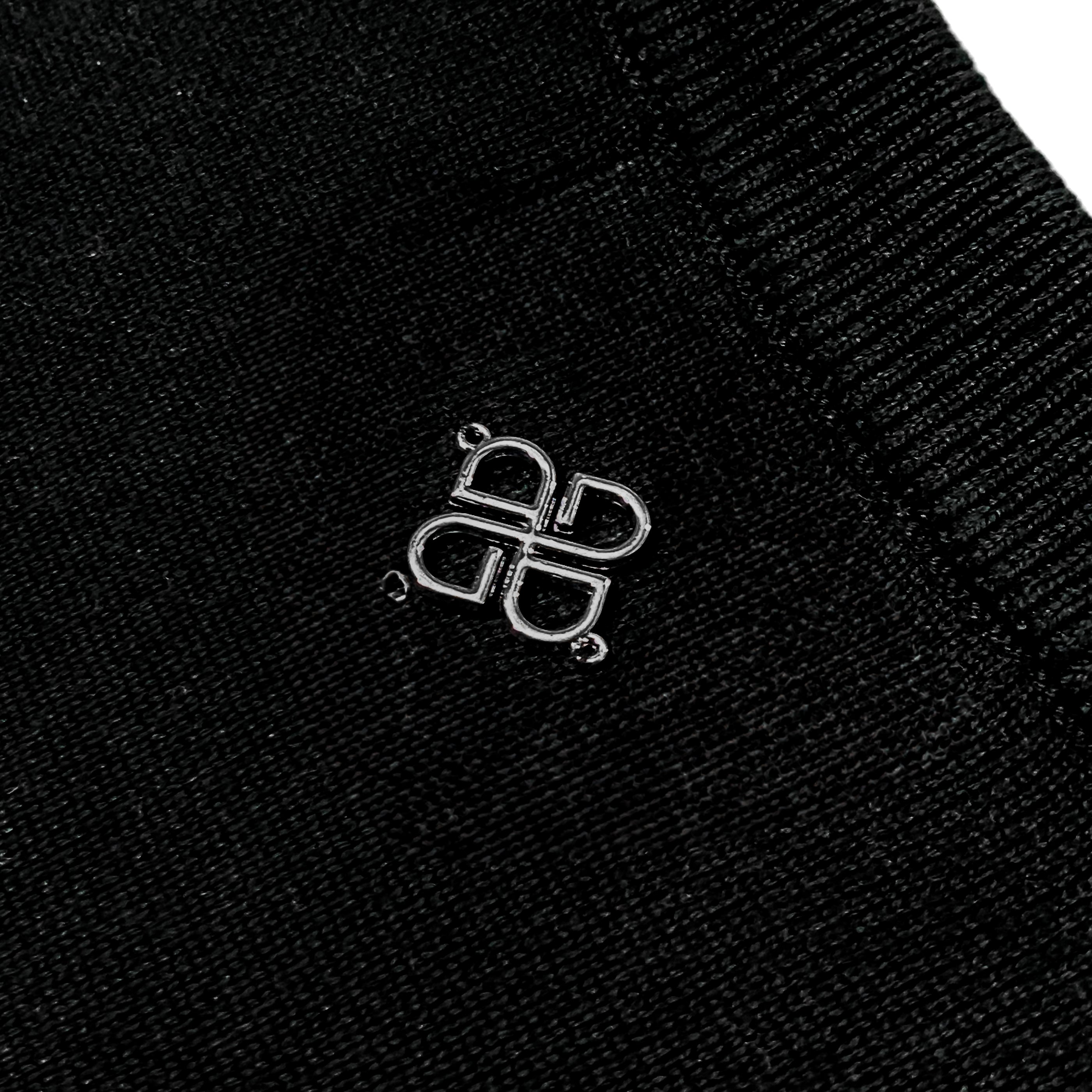 Close-up of black fabric with metallic emblem featuring four symmetrical loops and visible stitching