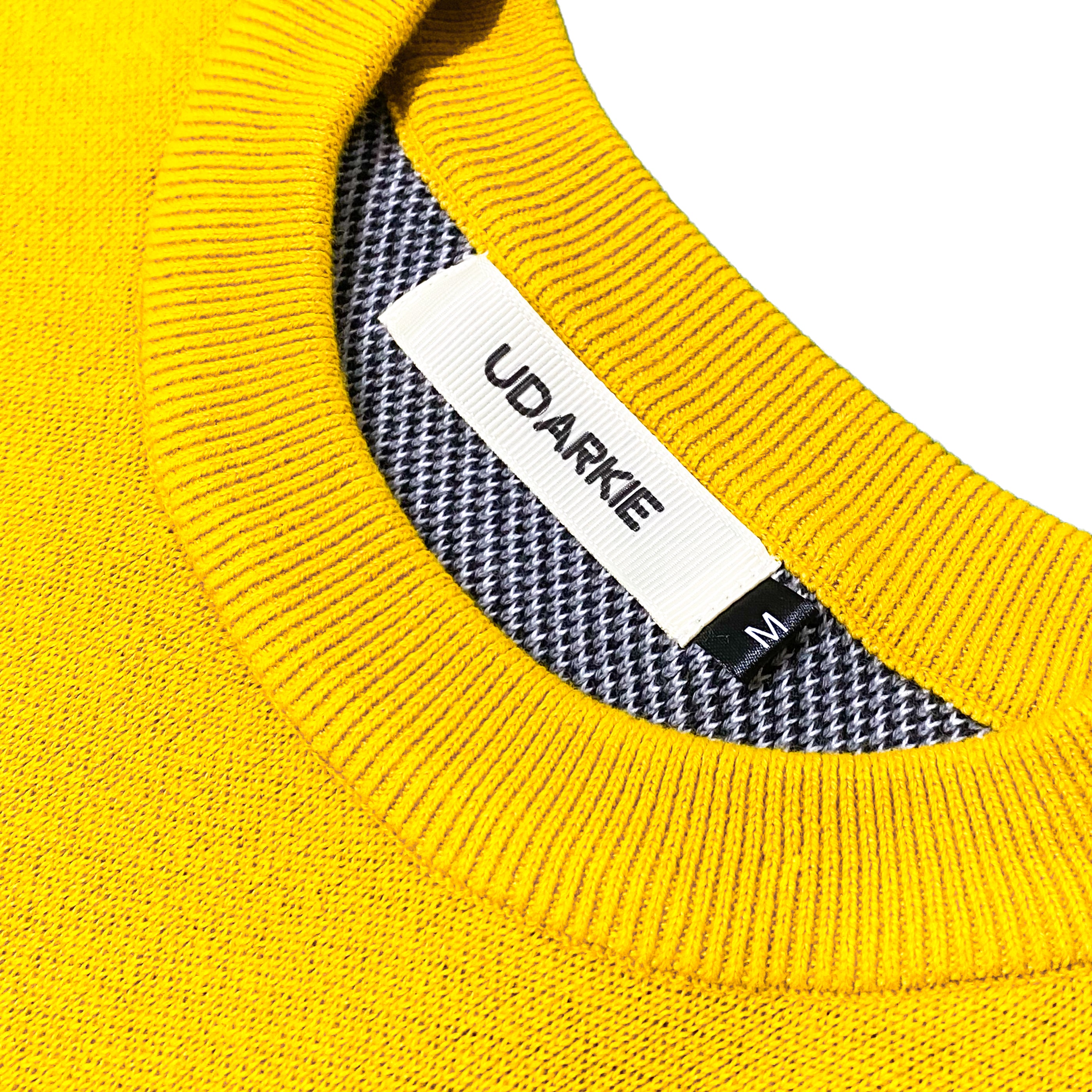 Close-up of yellow knitted sweater collar with UDARKIE label, size M tag, and black and white houndstooth inner lining