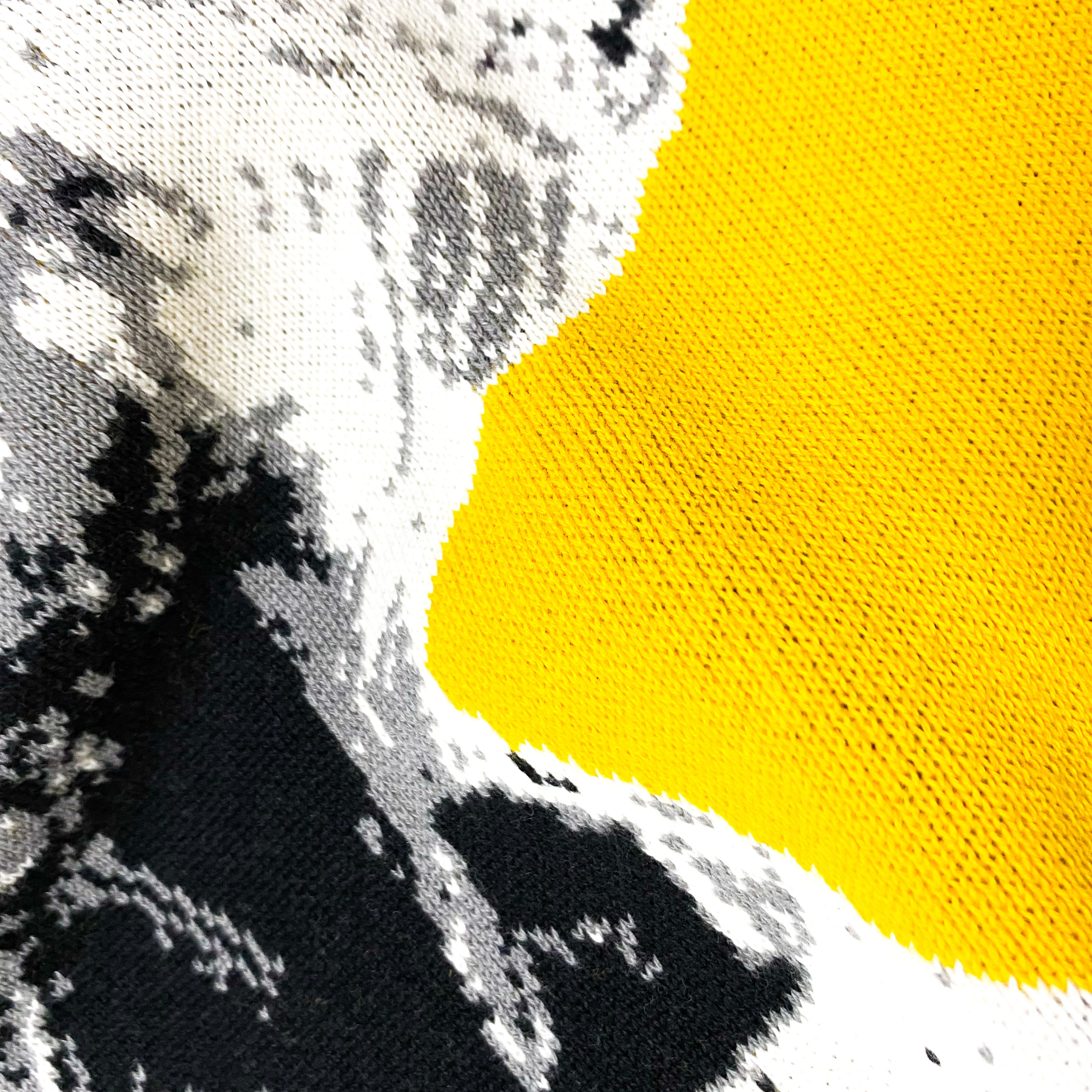 Close-up of knitted fabric with abstract black, white, and gray pattern next to solid yellow section