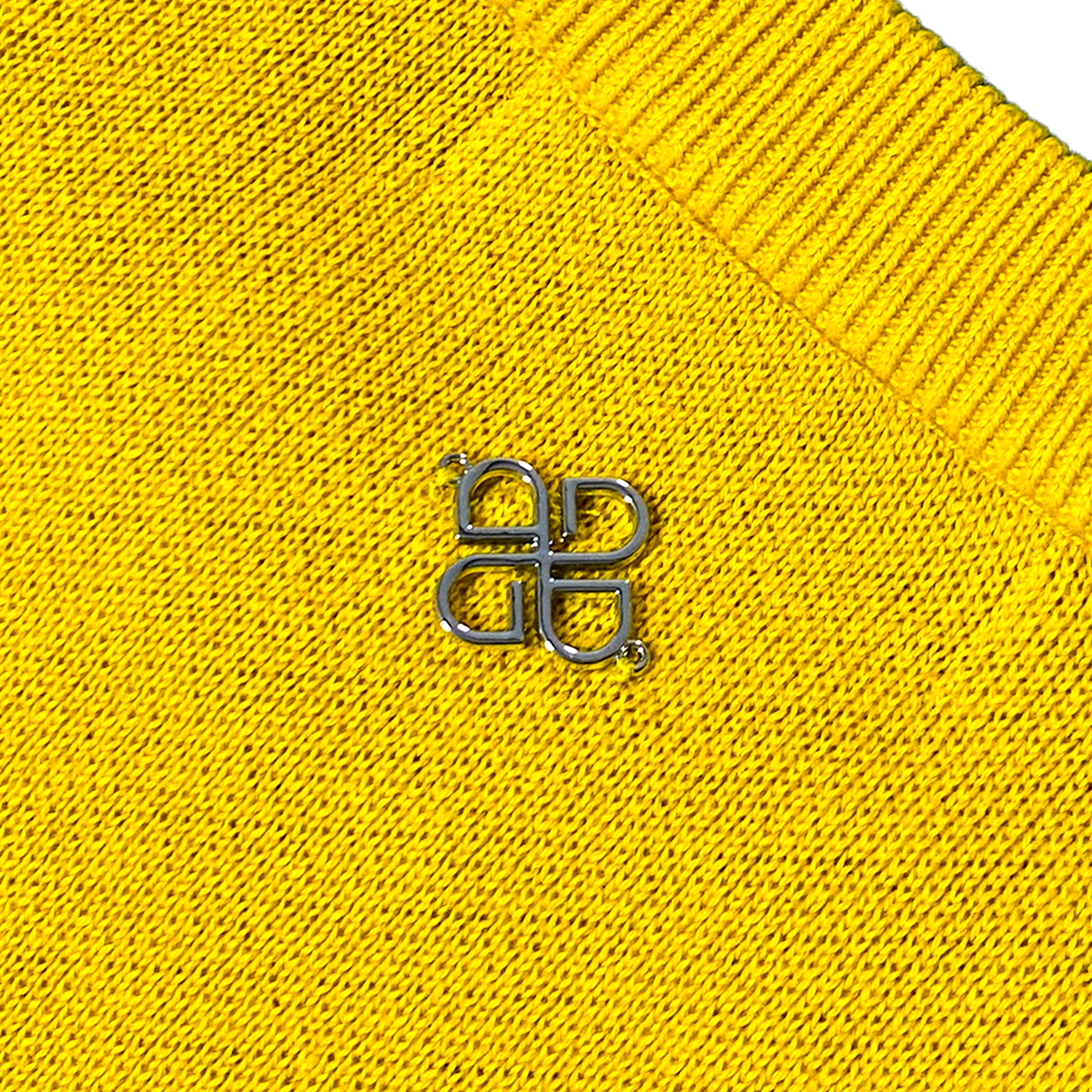 Close-up of yellow knitted fabric with ribbed edge and metallic emblem featuring interlocking shapes