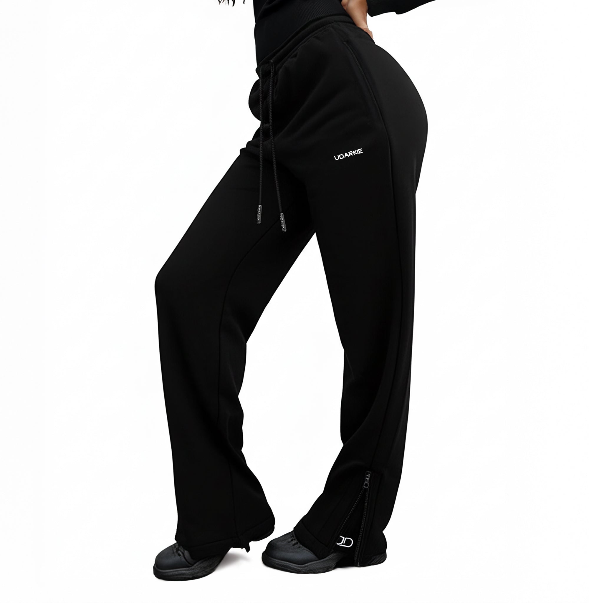 Black trackpants with drawstring waist, "UDARKIE" logo on upper thigh, and zippered ankles, worn with black shoes