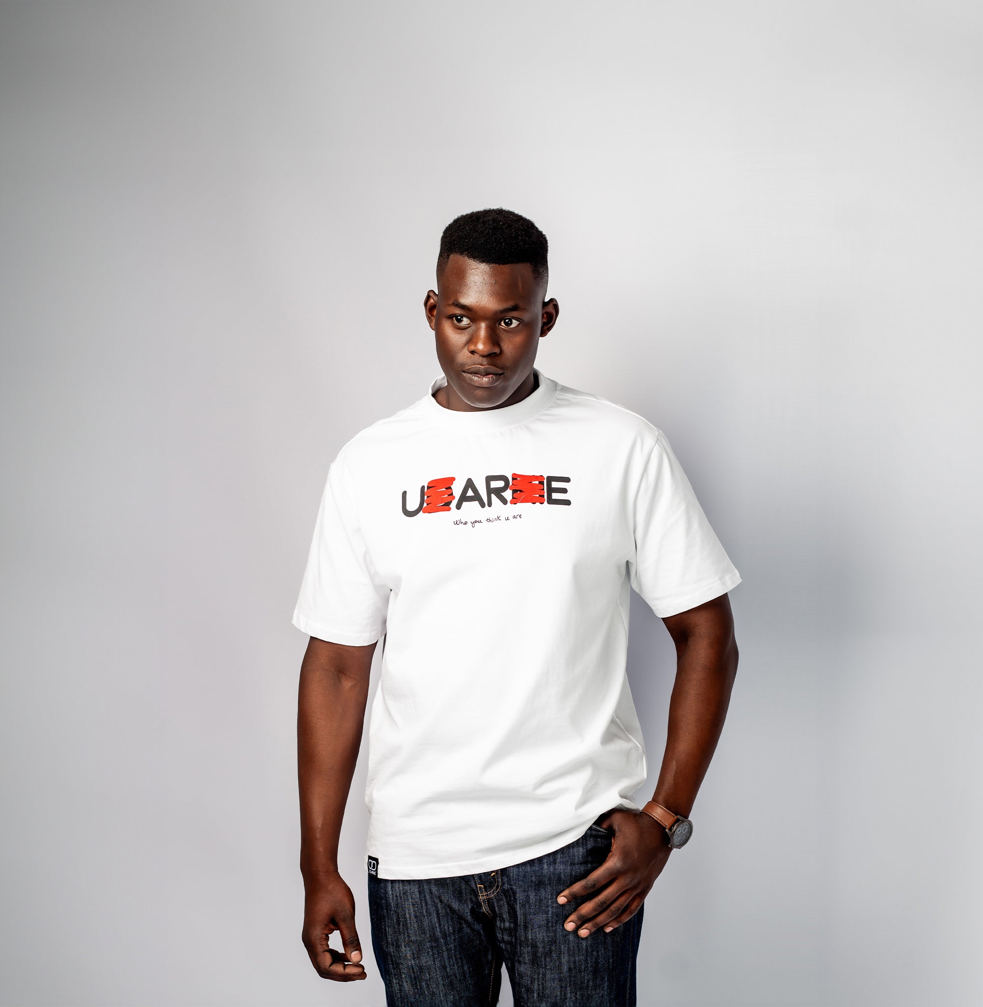 White T-shirt with "U ARE" text where "D" and "K" are crossed out in red to read "U ARE", and smaller text below saying "Who you think u are". Features UD LABEL branding at the neck and a small black tag at the bottom.