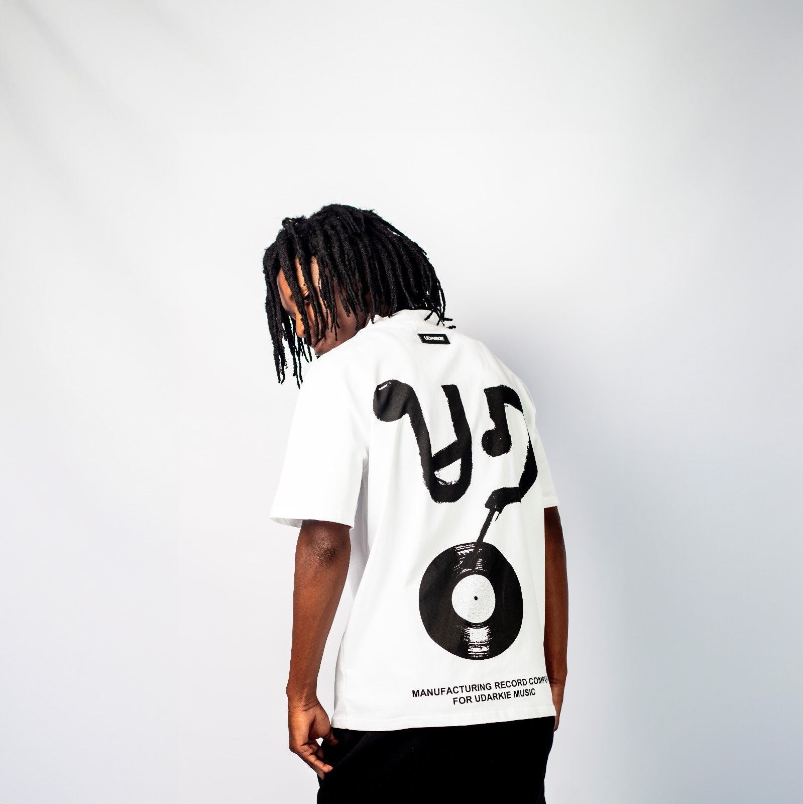 Back view of a white T-shirt featuring a black vinyl record graphic with stylized "U" and "D" shapes, and text reading "MANUFACTURING RECORD COMPANY FOR UDARKIE MUSIC".