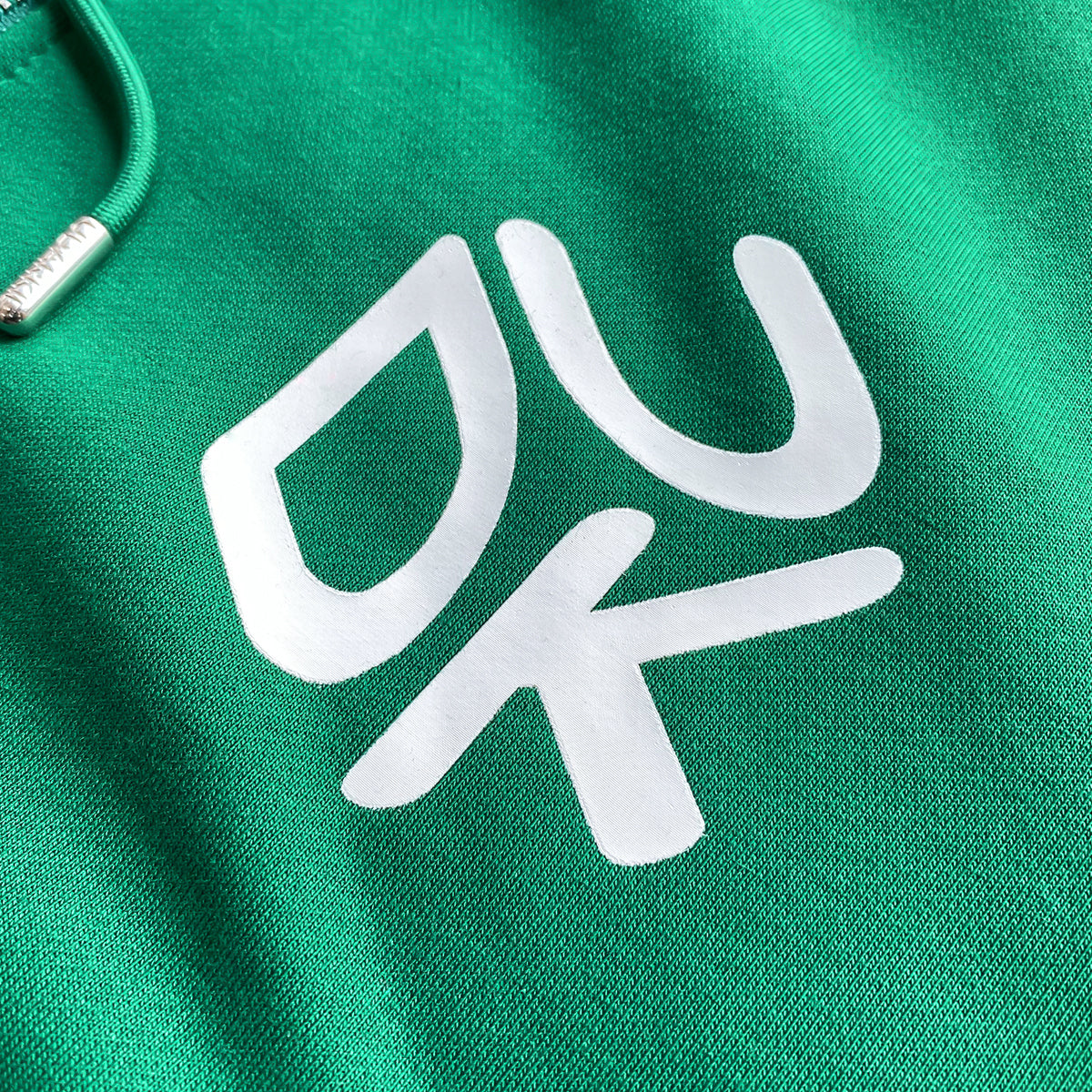 Close-up of green hoodie with white "UDK" logo and drawstring with a metal tip