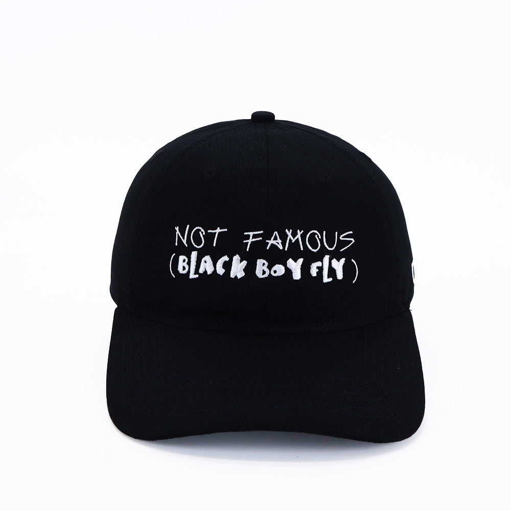 Black dad cap with white embroidered text reading “NOT FAMOUS (BLACK BOY FLY)” on the front.