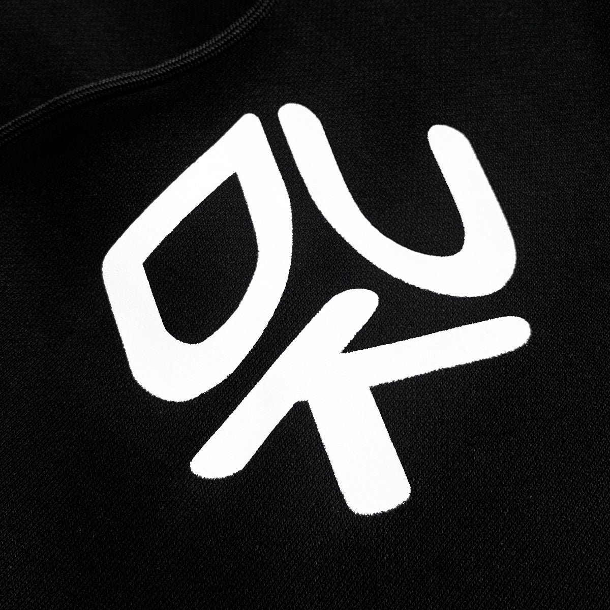 Close-up of black fabric with bold white graphic design with stylized letters "UDK"