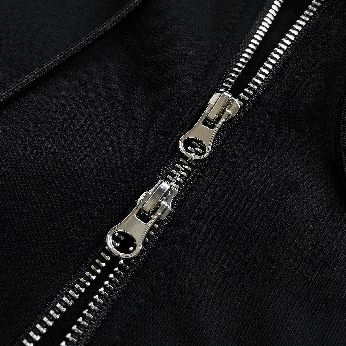 Close-up of black hoodie with two parallel metallic zippers partially unzipped, showing interlocking teeth