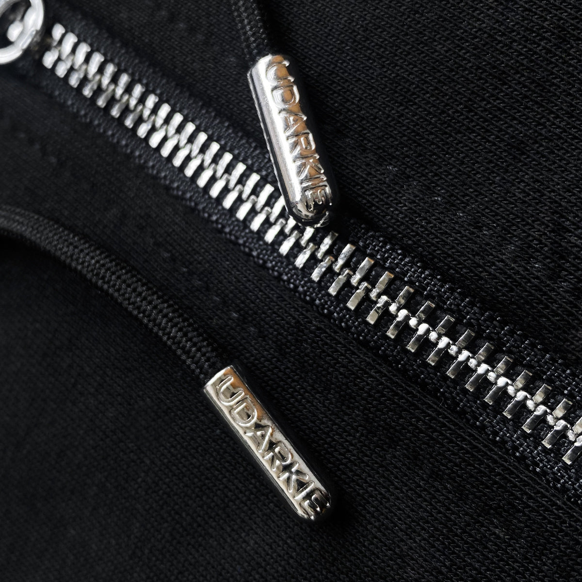 Close-up of black hoodie with silver zipper and UDARKIE branded drawcords