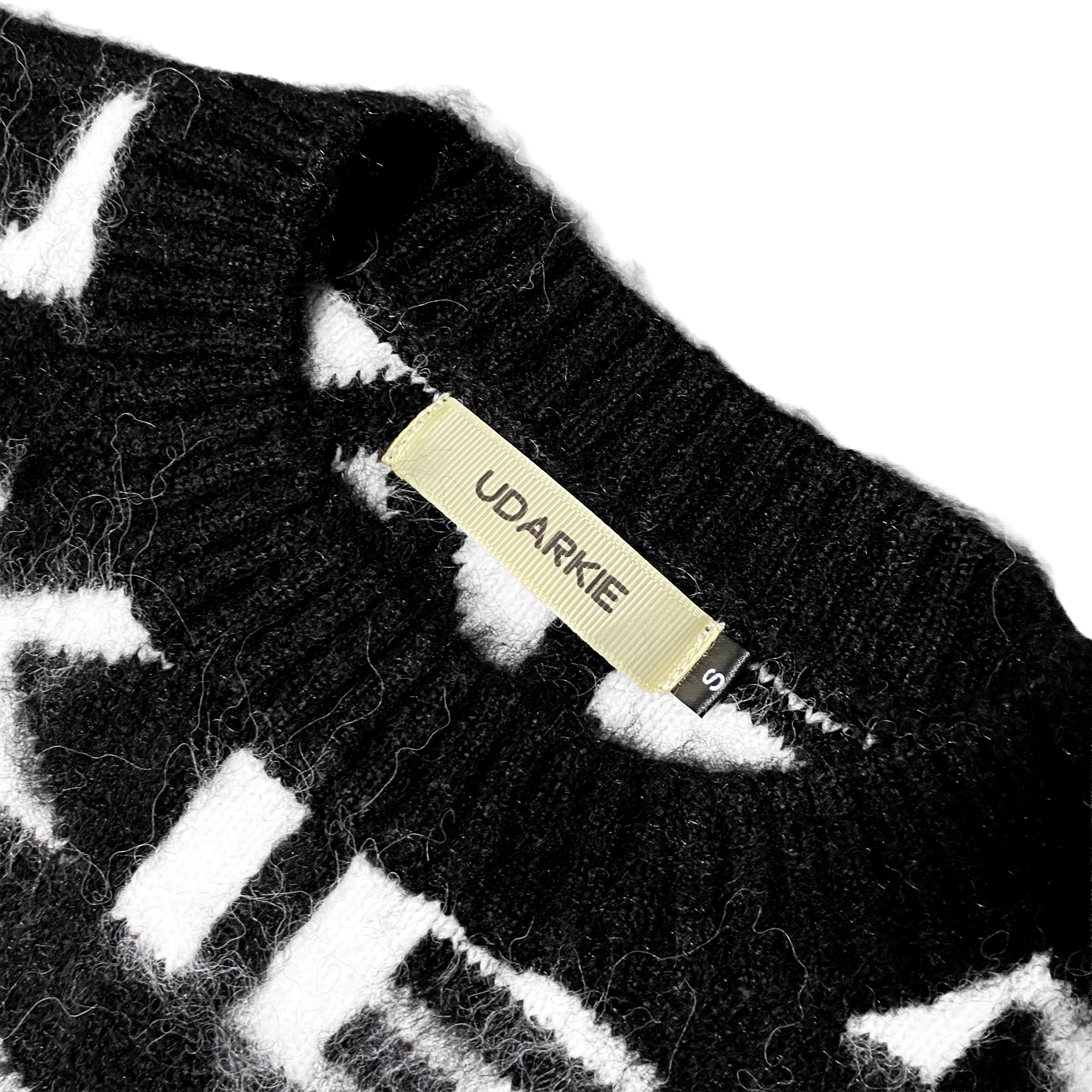 Close-up of the collar of a black and white knitted garment with a fuzzy texture, featuring a "UDARKIE" brand label and size tag marked "S".