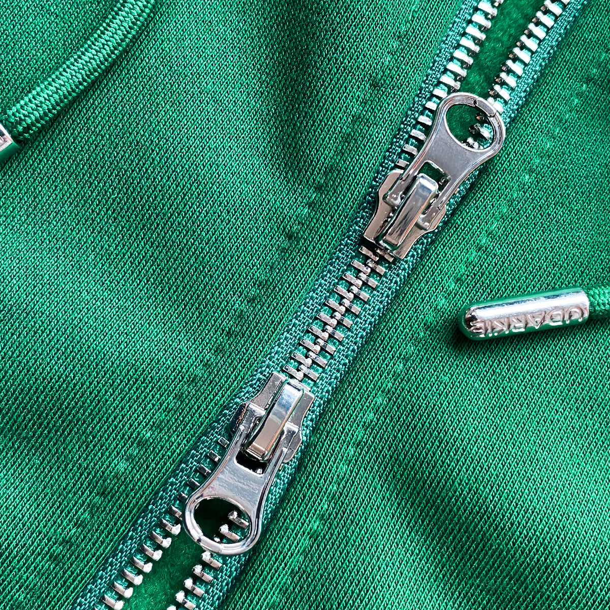 Close-up of green hoodie with two parallel metallic zippers partially unzipped, showing interlocking teeth