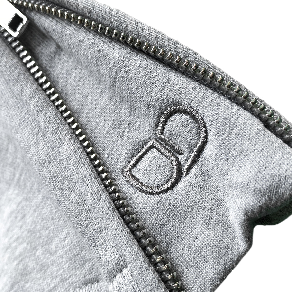 Close-up of gray trackpant with a zipper at the bottom and gray embroidered "UD" logo near the edge.
