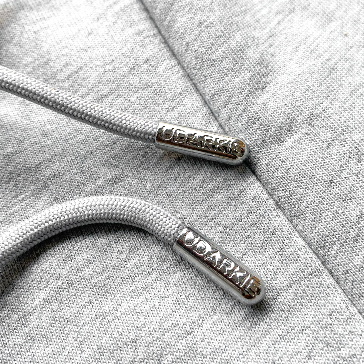 Close-up of gray sweatpants drawstring aglets engraved with the brand name "UDARKIE"