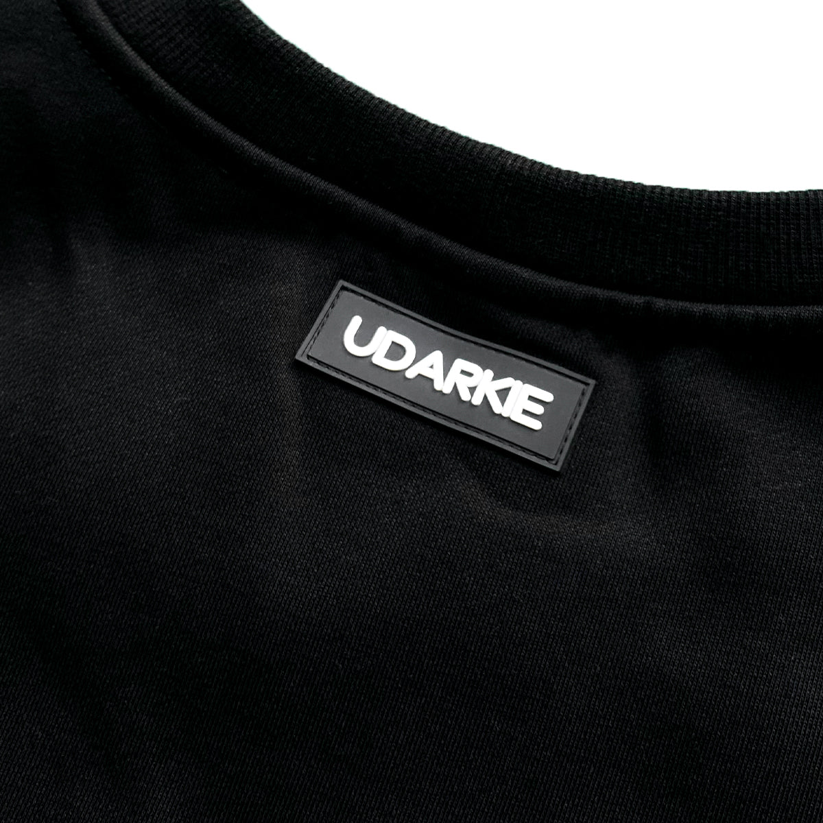 Close-up of black shirt neckline with sewn "UDARKIE" label in white capital letters.