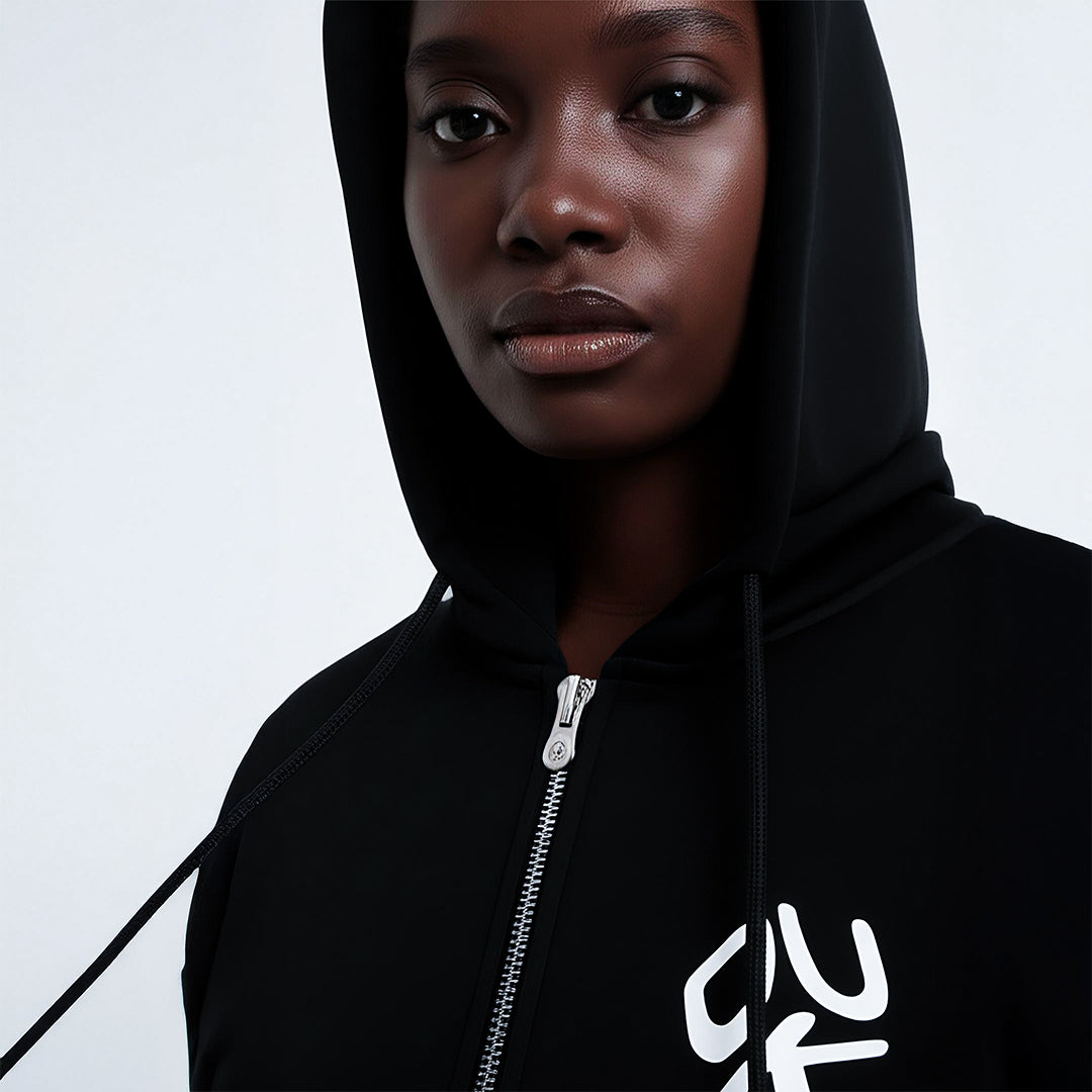 Front view of a women wearing a black zip-up hoodie with white graphic design on the left chest area
